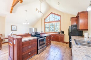 A kitchen with a central island, wooden cabinets, a stainless steel refrigerator, and a large window providing natural light.