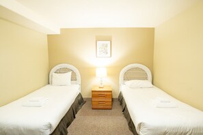 A room with two single beds, a nightstand with a lamp, and a framed picture on the wall.