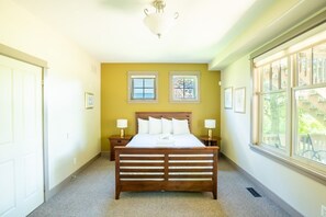 A bedroom with a wooden bed, two bedside tables with lamps, a ceiling light fixture, and two windows with blinds. - The Vista at Blue View Chalets (The Blue Mountains)