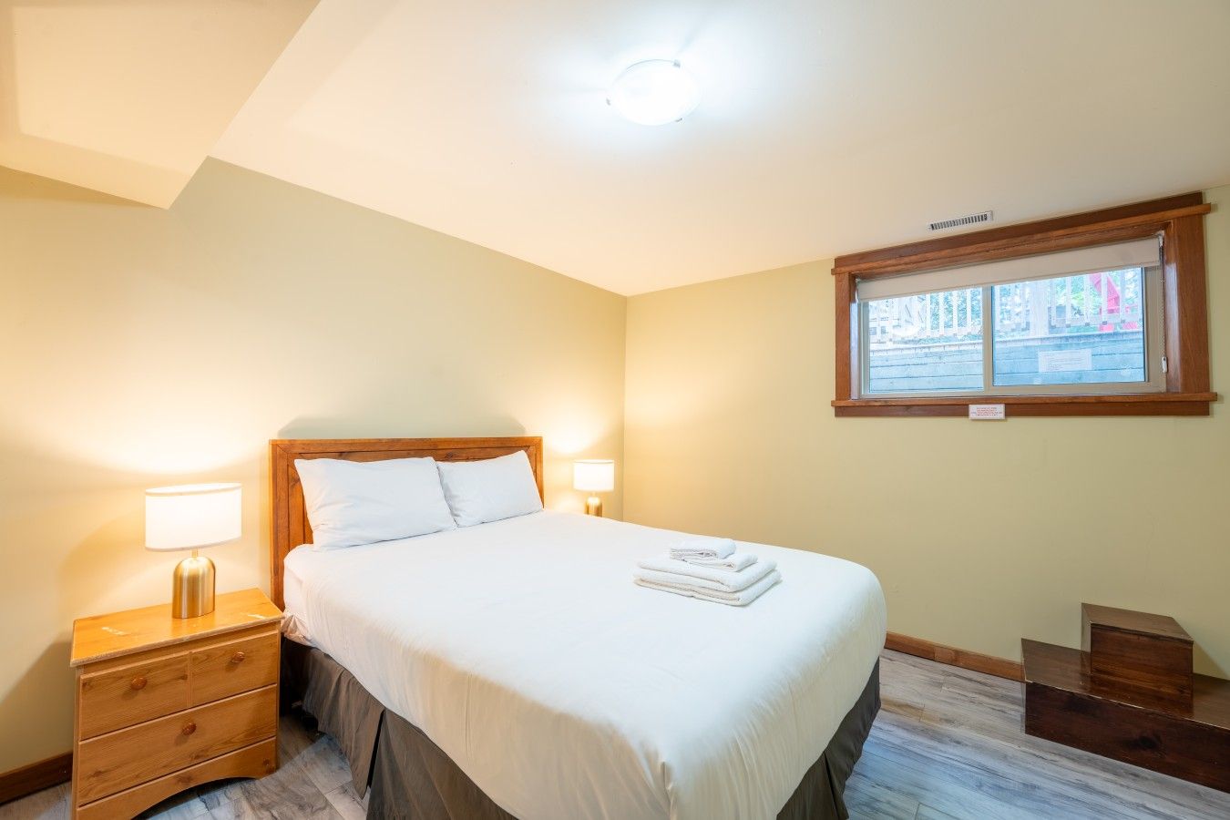 Une chambre à coucher avec un lit, des lampes de chevet, une fenêtre et une table de chevet en bois.