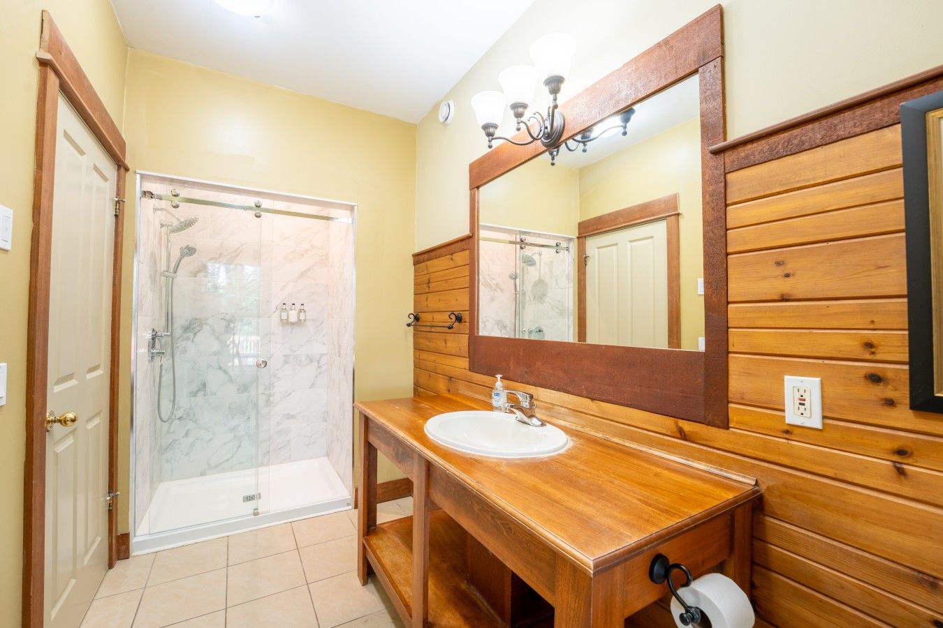 A bathroom with a wooden vanity, a marble shower enclosure, and a large mirror.