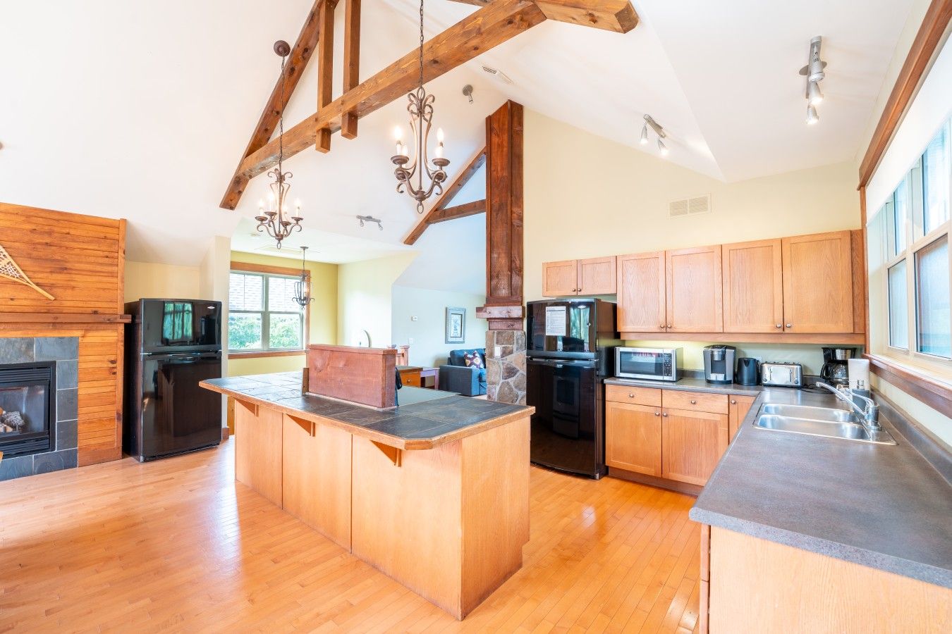 A spacious kitchen with a central island, wooden cabinets, and a stone fireplace.