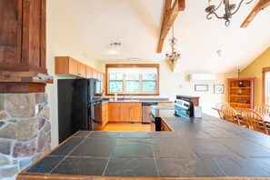 A kitchen with a stone wall, wooden cabinets, a black refrigerator, a stove, and a dining area with chairs.