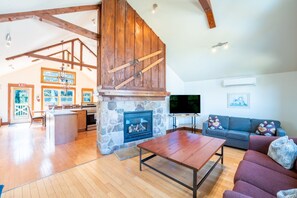 A spacious living area with a stone fireplace, wooden beams, a television, and a sofa. - The Vega at Blue View Chalets (The Blue Mountains)