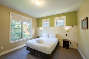 A bedroom with a large bed, two windows, a nightstand, and a wall-mounted lamp. - The Corona at Blue View Chalets (The Blue Mountains)