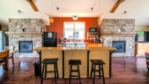 A kitchen with a stone fireplace, wooden beams, and a central island with stools. - The Stella at Blue View Chalet (The Blue Mountains)
