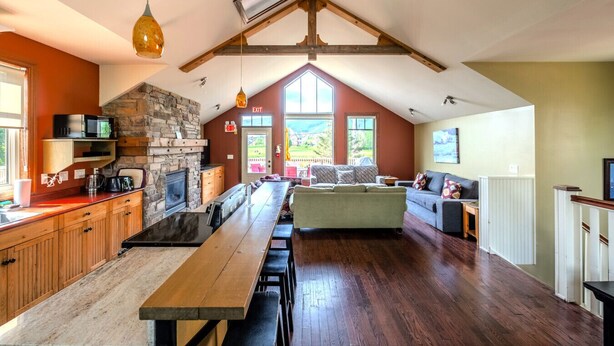 A spacious kitchen with a stone fireplace, wooden cabinets, and a long dining table. - The Stella at Blue View Chalet (The Blue Mountains)