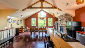 A spacious kitchen with a stone fireplace, wooden beams, and a long dining table. - The Stella at Blue View Chalet (The Blue Mountains)