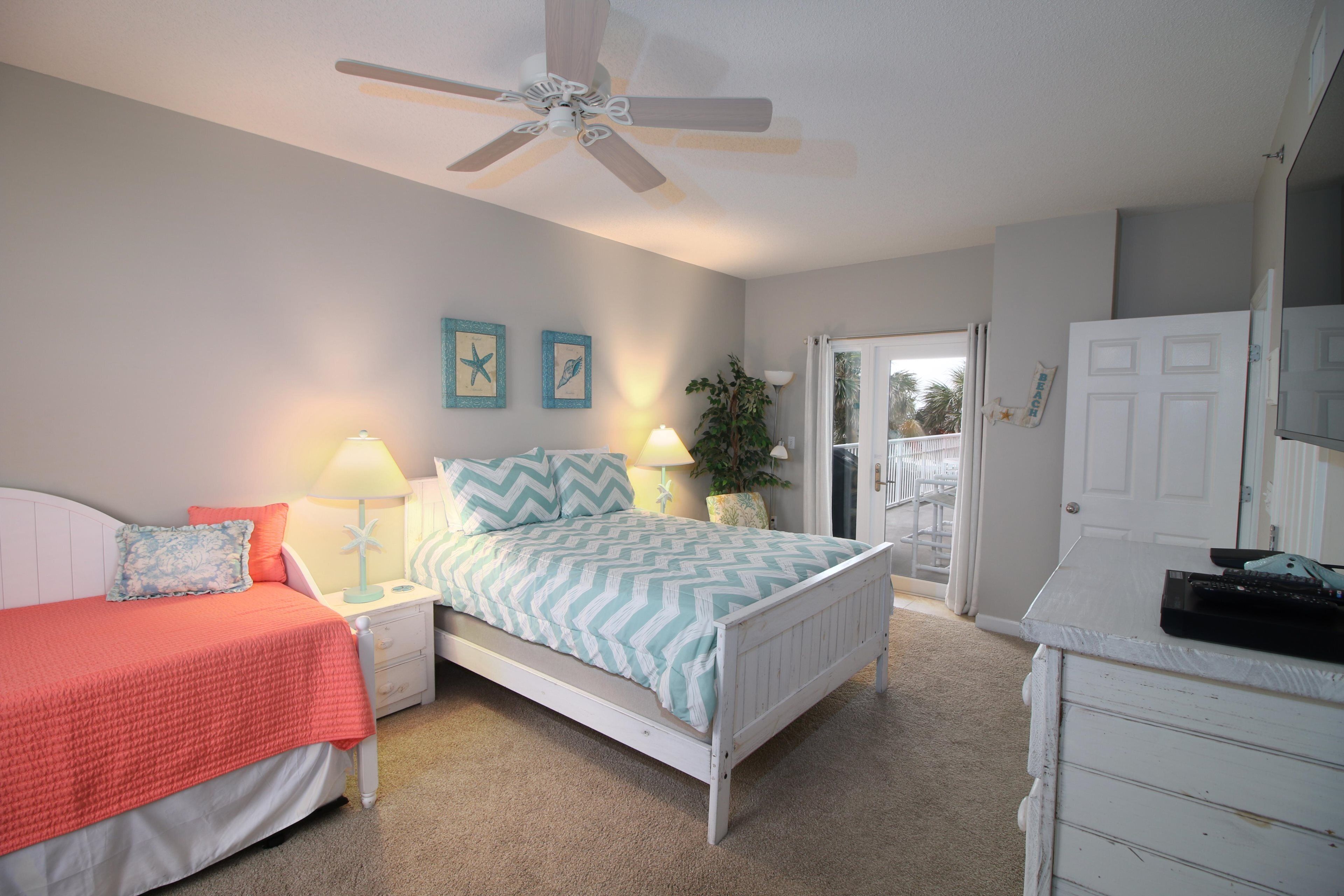 A bedroom with a bed, two bedside tables with lamps, a ceiling fan, and a door leading to a balcony.