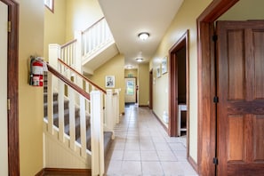 A hallway with a staircase, wooden doors, and a fire extinguisher.
