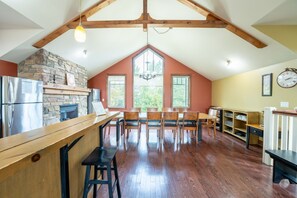 A spacious kitchen with a stone fireplace, wooden dining table, and chairs, with a large window providing a view of the outdoors.