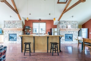 Una cocina con chimenea de piedra, vigas de madera y una isla grande con taburetes.