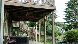 Eine Holzterrasse mit Whirlpool, einem Stuhl und einer Treppe zu einem überdachten Bereich.