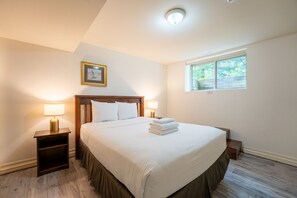 A bedroom with a large bed, two bedside lamps, a framed picture on the wall, and a window. - The Prima at Blue View Chalets (The Blue Mountains)