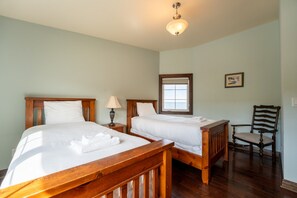 Une chambre avec deux lits en bois, une table de chevet avec une lampe, une chaise et une fenêtre donnant sur un beau paysage.