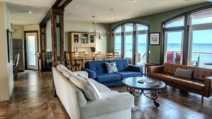 Un salon spacieux doté d’une grande fenêtre offrant une vue sur l’océan, un coin repas avec des meubles en bois et une cuisine équipée d’un réfrigérateur.
