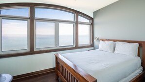 Une chambre avec une grande baie vitrée, un lit en bois et un mur blanc.