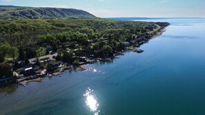 An aerial view of a lakeside community with houses along the shore, a dock, and a forested hillside in the background.