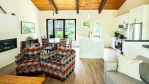 A spacious living area with a dining table, two sofas, a kitchen with modern appliances, and a large window offering a view of greenery. - The 44L at Blue View Chalets (The Blue Mountains)