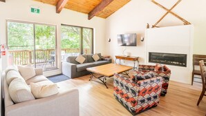 A spacious living area with a wooden ceiling, a fireplace, a television, and a balcony with outdoor seating. - The 44L at Blue View Chalets (The Blue Mountains)