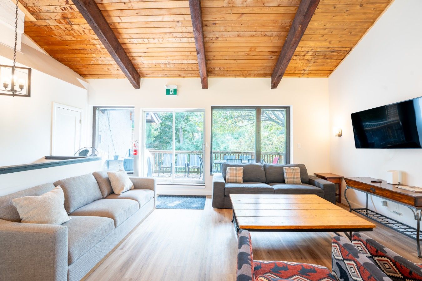 A spacious living area with a wooden ceiling, a sofa set, a coffee table, and a television mounted on the wall.