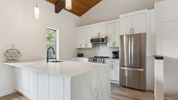 A modern kitchen with white cabinetry, a large island, stainless steel appliances, and a wooden ceiling. - The 44L at Blue View Chalets (The Blue Mountains)