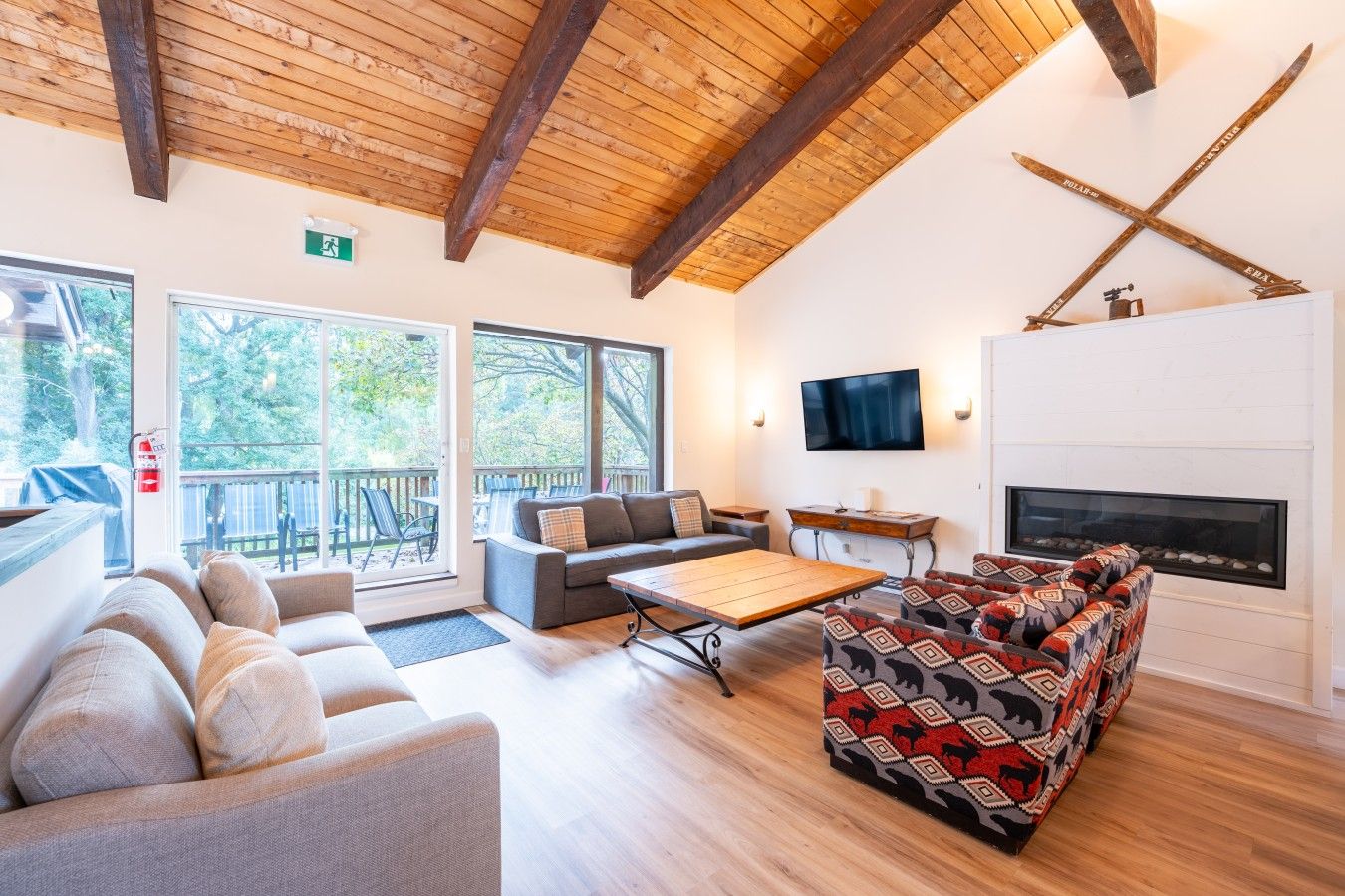 A spacious living area with a fireplace, a television mounted on the wall, and a large window overlooking a deck.