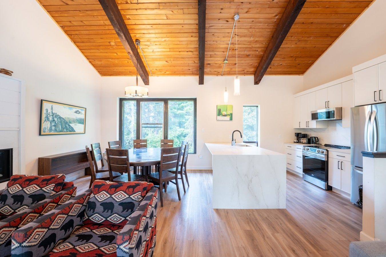 A modern kitchen with a central island, wooden beams on the ceiling, and a dining area with a patterned rug.