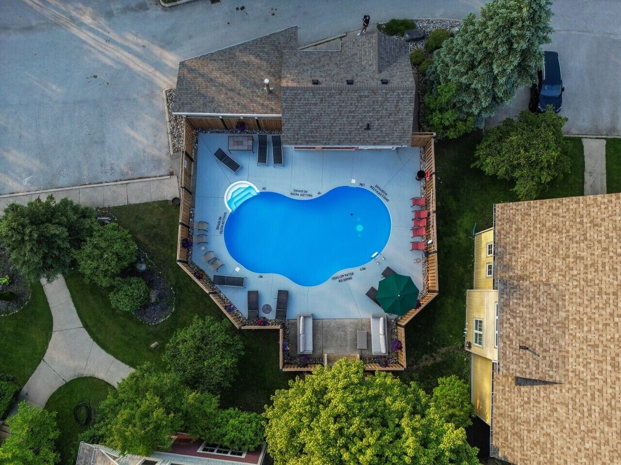 An aerial view of a residential property with a swimming pool, surrounded by a deck and lounge chairs.