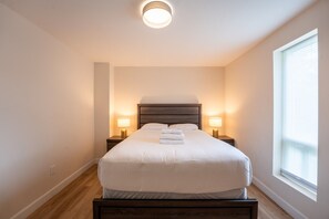 A neatly made bed in a room with a large window, two bedside lamps, and a ceiling light. - The 44L at Blue View Chalets (The Blue Mountains)