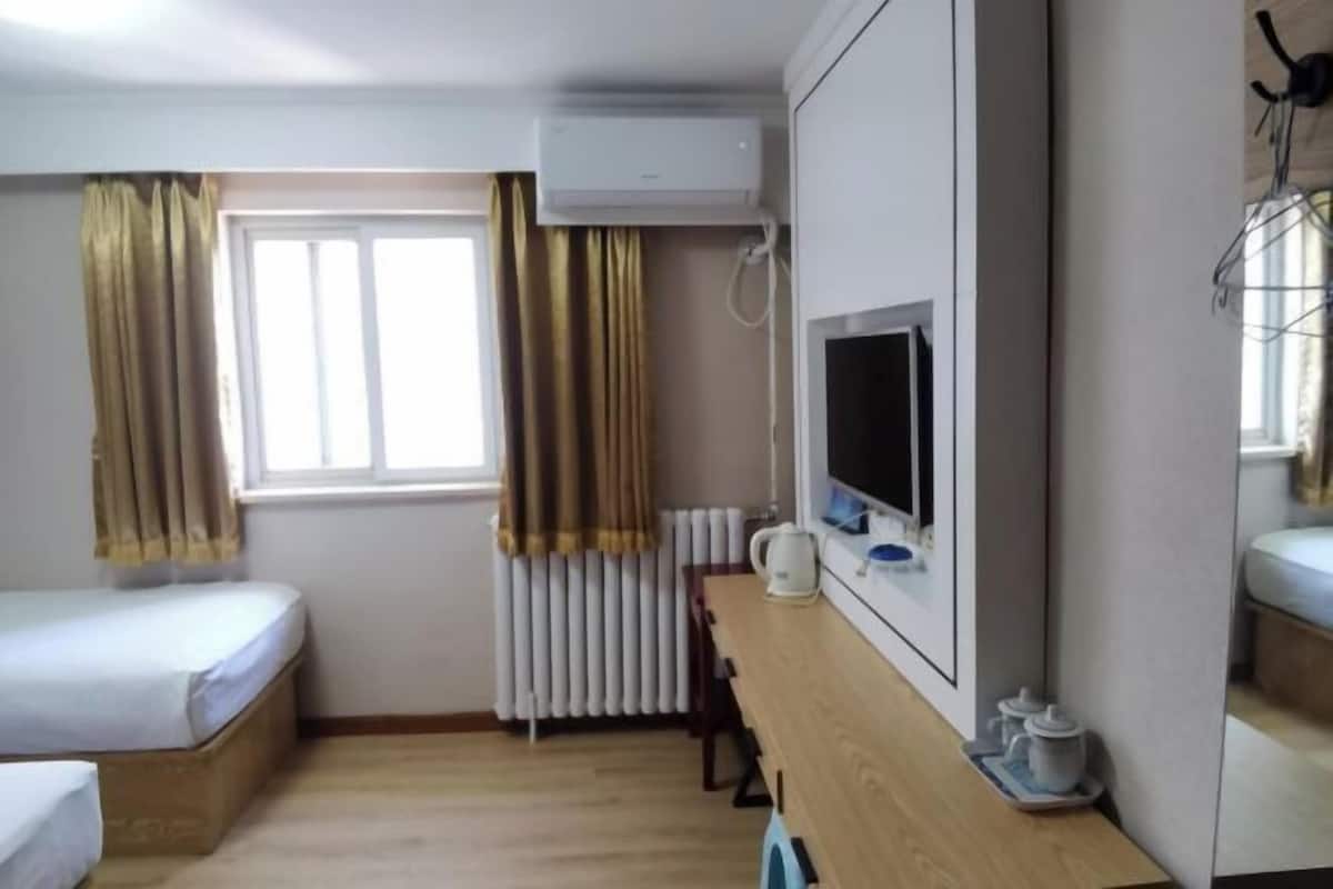 A hotel room with a bed, a desk with a computer, a radiator, and a window with curtains.