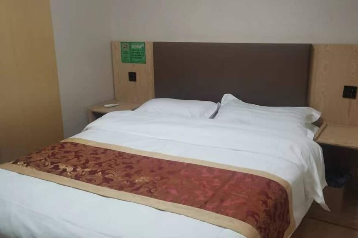 A hotel room with a bed, a nightstand, a wooden headboard, and a green sign on the wall.