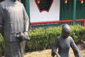 A statue of a person in traditional attire standing next to a building with green and red trim. - Huawei Hotel (Headquarters Base Yungang Road Branch) (Beijing)