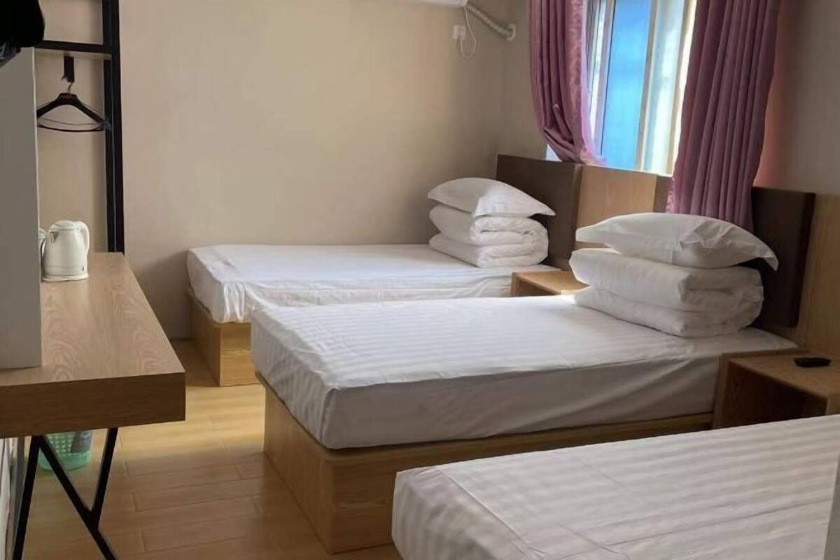 A hotel room with two beds, a wooden desk, a hanging coat rack, and a window with curtains.