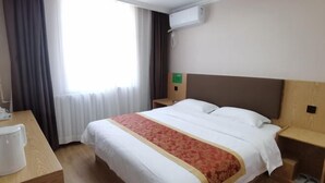 Ein Hotelzimmer mit Bett, Nachttisch, Kaffeemaschine, einem Fenster mit Vorhängen und einer Klimaanlage.