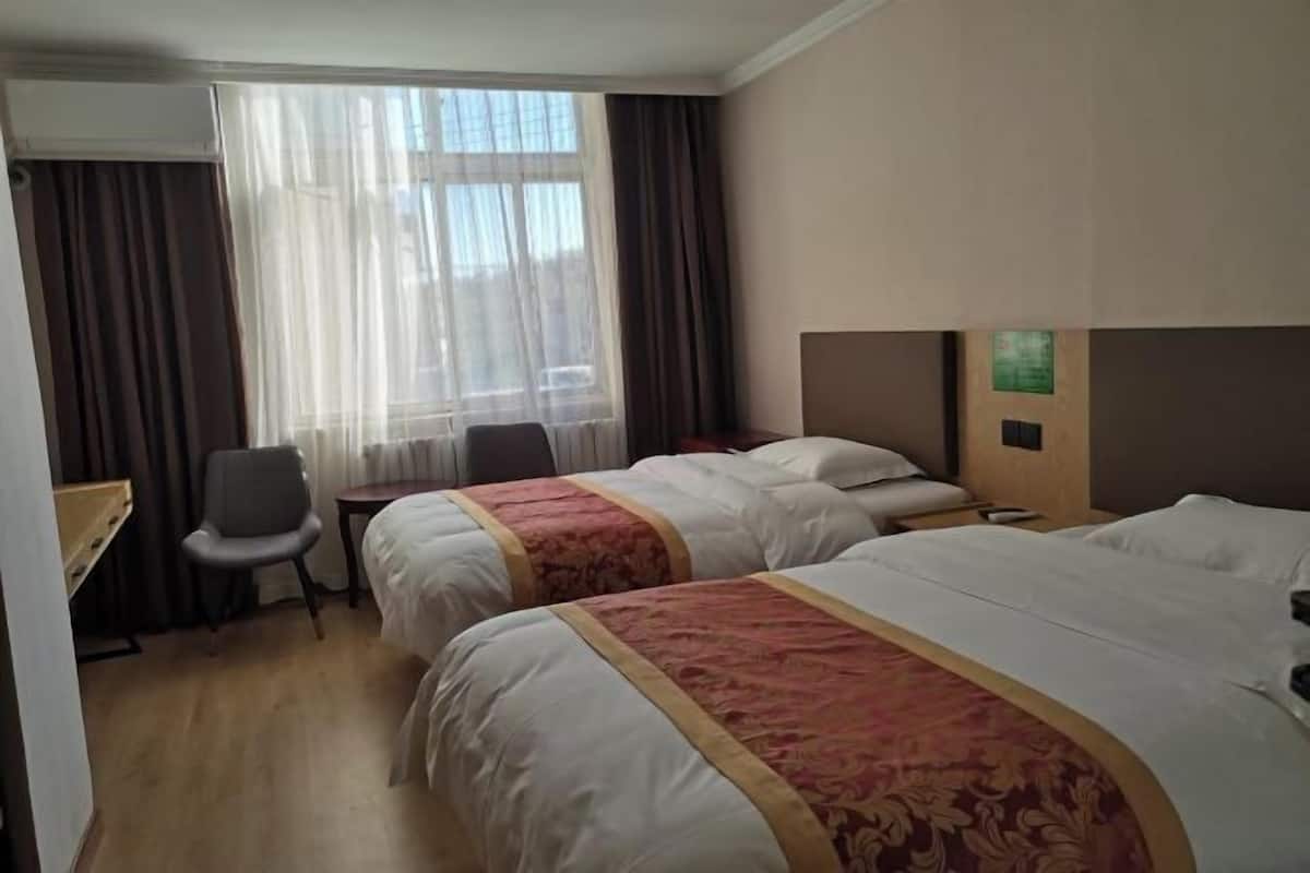 A hotel room with two beds, a desk, a chair, and a window with curtains.