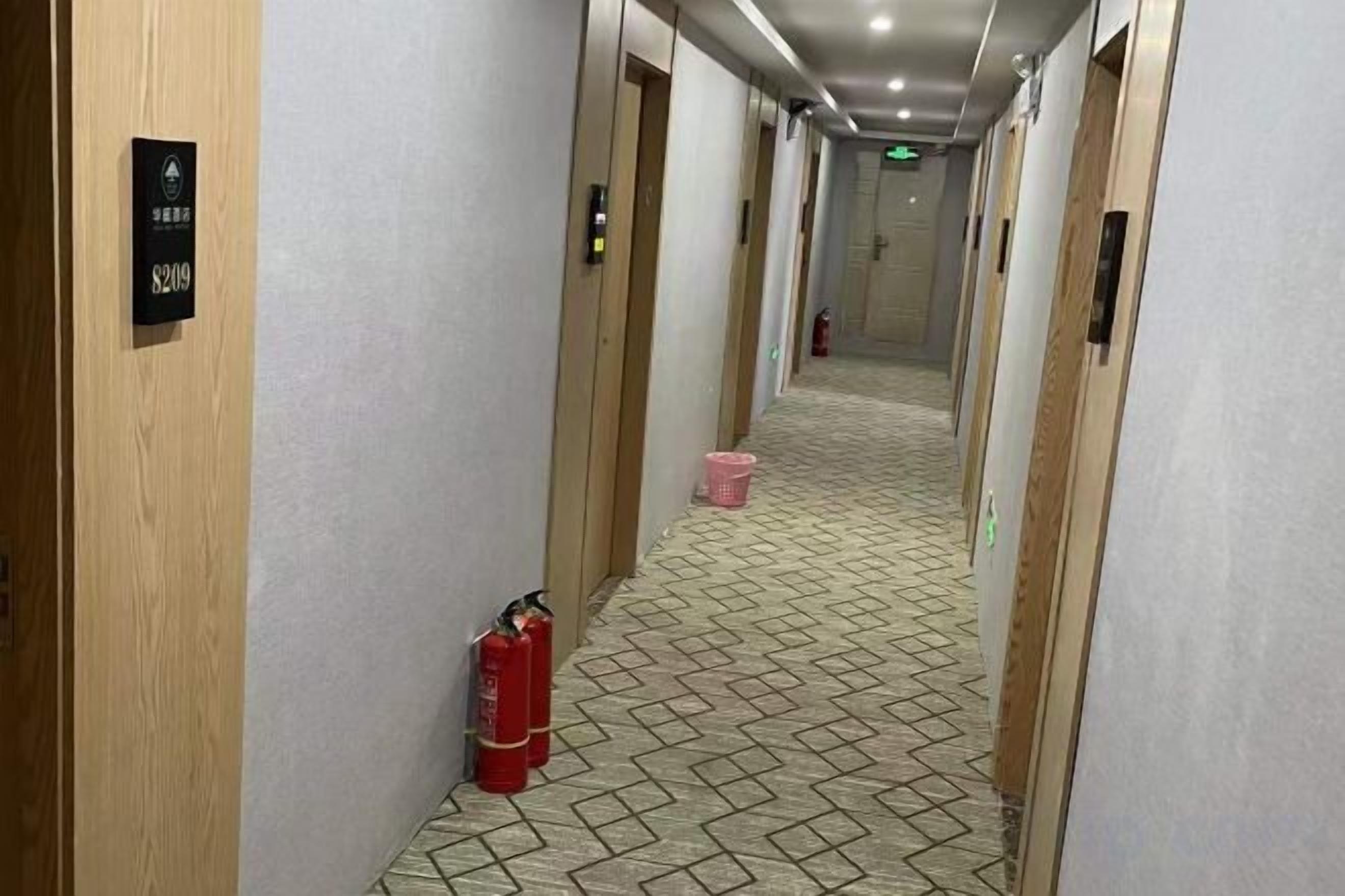 En hotellkorridor med trädörrar, en brandsläckare och ett mönstrat golv.