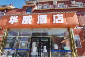 A hotel entrance with a glass facade and a red awning displaying the name '华威酒店'. - Huawei Hotel (Headquarters Base Yungang Road Branch) (Beijing)