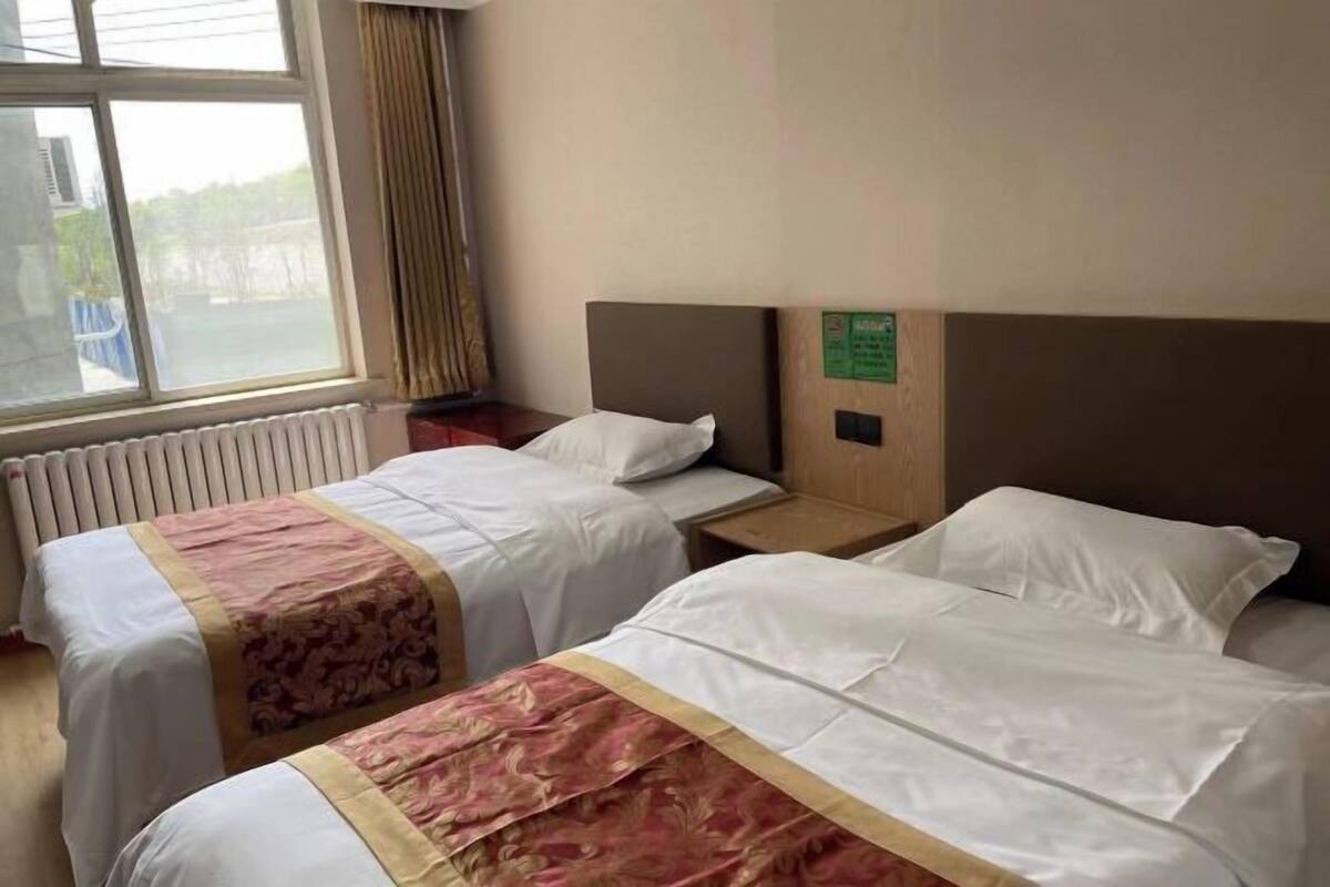 A hotel room with two beds, a window with curtains, a radiator, and a sign on the wall.