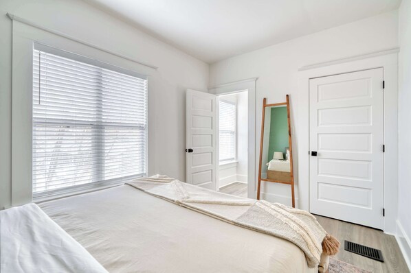 A bedroom with a large bed, white walls, and a wooden ladder leaning against a door.