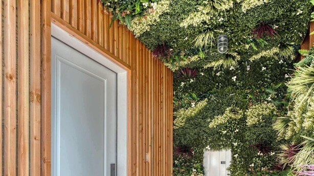 A wooden door with a white panel, a tiled patio, and a wall covered with various plants and greenery. - Mississippi Ave Compound | 7BR • Sleeps 14 (Portland)
