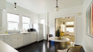 A modern kitchen with white cabinets, a stainless steel sink, and a round dining table with gold chairs. - Mississippi Ave Compound | 7BR • Sleeps 14 (Portland)