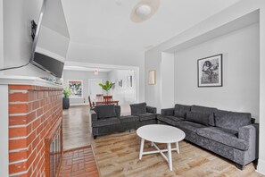 A modern living room with a sectional sofa, a small white table, and a brick wall. - Remodeled 3BR - Walk to Coffee, Bars & More (Portland)