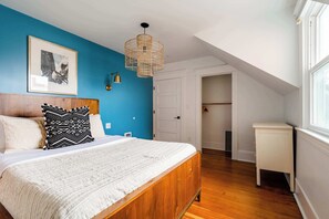 A bedroom with a wooden bed, a white bedside table, a blue accent wall, a hanging light fixture, and a framed picture on the wall.