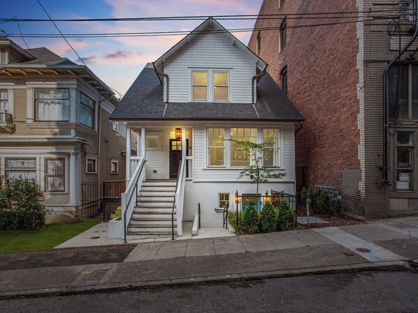 A two-story house with a front porch, a staircase, and a small tree in the front yard.