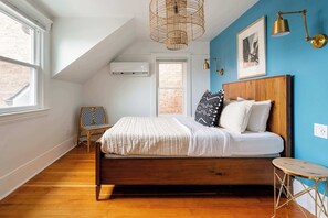 A bedroom with a wooden bed, a chair, a small table, a hanging light fixture, and a window. - Sophisticated 3BR - Prime NW 23rd Location (Portland)