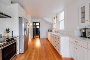 A modern kitchen with white cabinetry, stainless steel appliances, and a wooden floor.