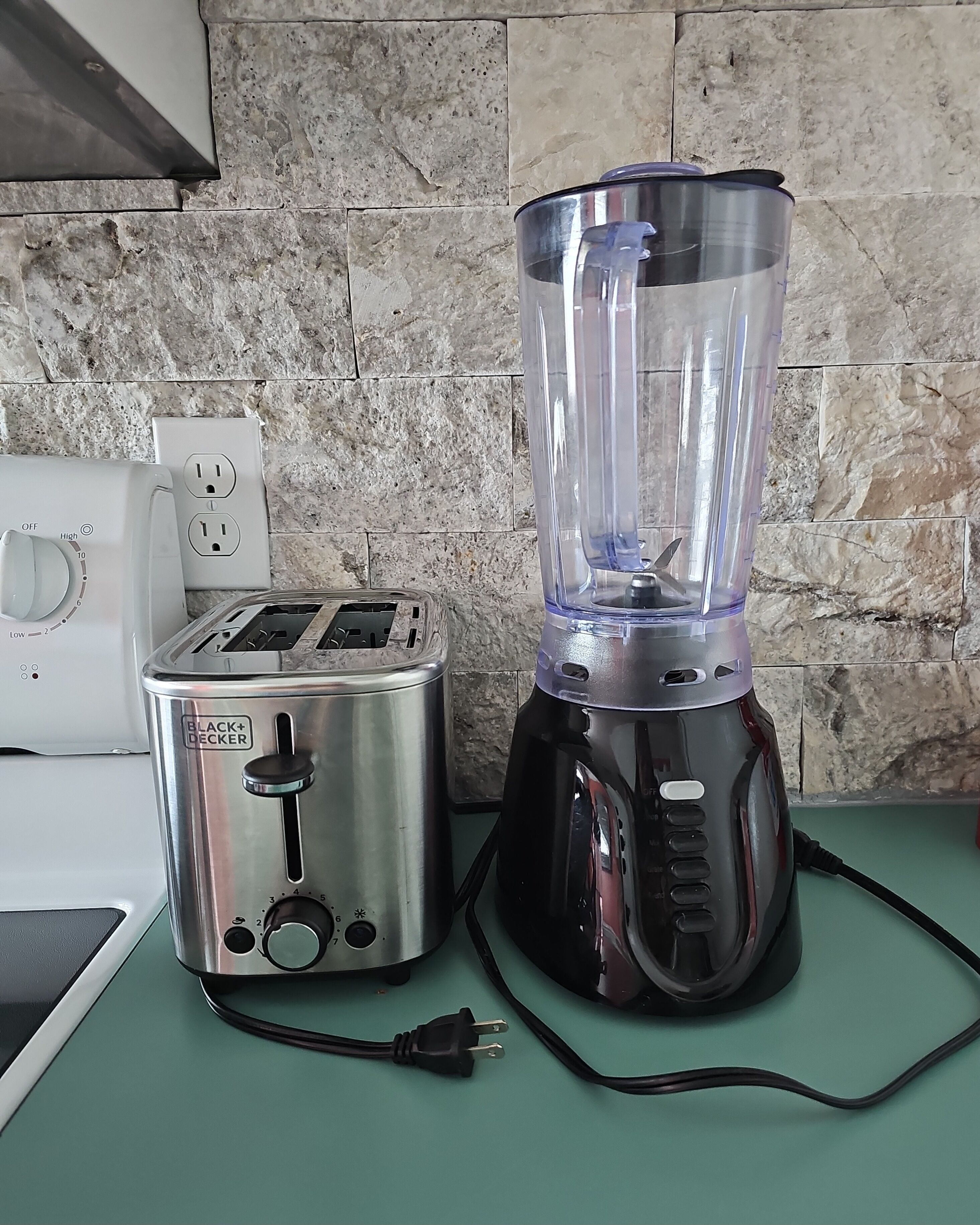 A kitchen with a toaster, a blender, and a stone backsplash.