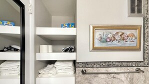 Un baño con cabina de ducha azulejada, un perchero y un cuadro concaracoles en la pared.