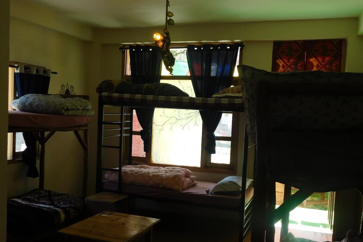 Une chambre de dortoir avec des lits superposés, une petite table et une fenêtre avec des rideaux.